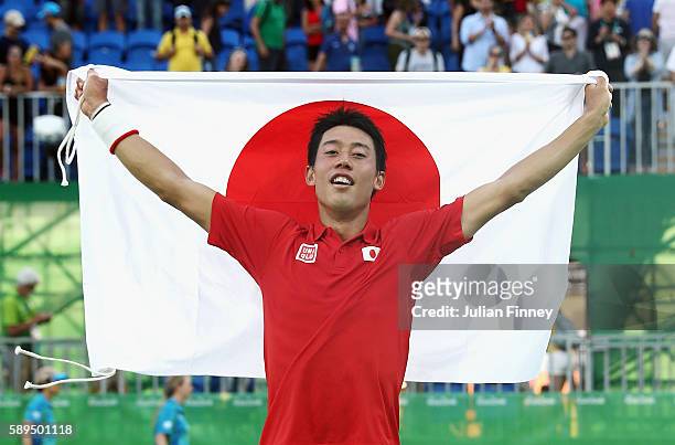 Kei Nishikori of Japan celebrates with the Japanese flag after winning the singles bronze medal match against Rafael Nadal of Spain on Day 9 of the...