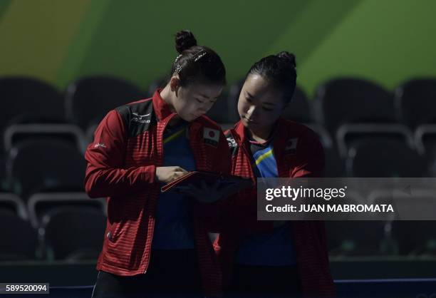 Japan's Mima Ito and teammate Japan's Ai Fukuhara look at a tablet computer as another team member Japan's Kasumi Ishikawa plays against Germany's...