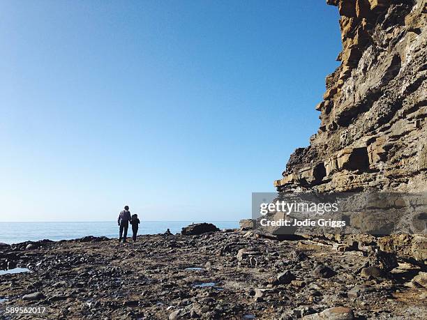 girl walking with grandfather beside a large cliff - beach clear sky stock pictures, royalty-free photos & images