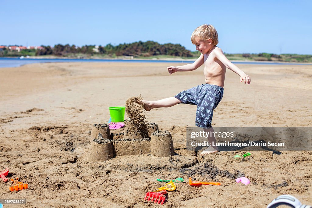 Boy kicking against sandcastle on beach