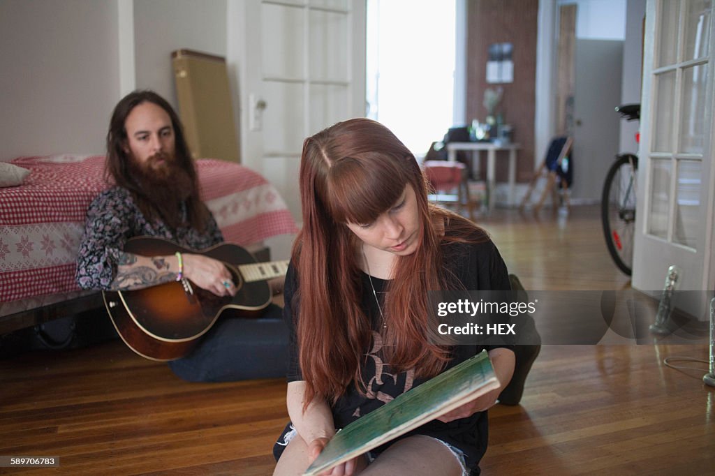 Young woman looking at a record album while her boyfriend plays guitar