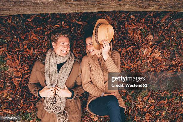 young couple lying side by side on autumn leaves in an park - couple love stock-fotos und bilder