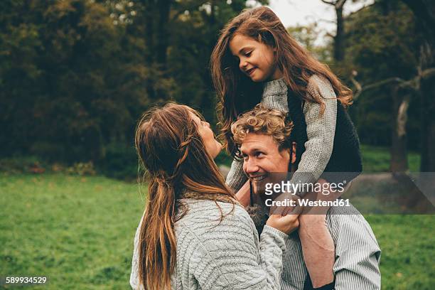 happy young couple with little girl on her father's shoulders at autumnal park - mann mit kind auf den schultern stock-fotos und bilder