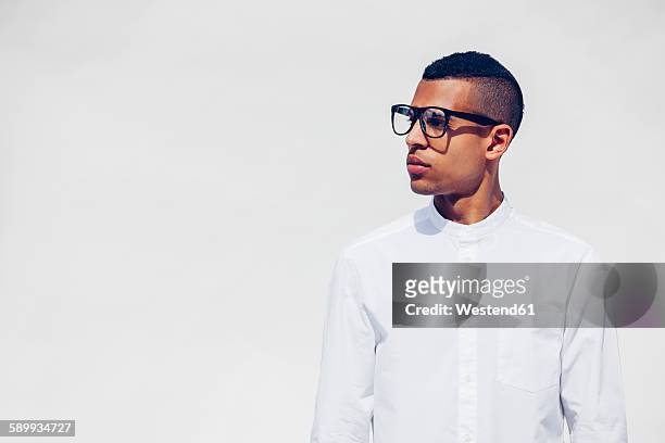 portrait of young man with shaved hair and glasses wearing white shirt in front of white background - white/black shirt stock-fotos und bilder