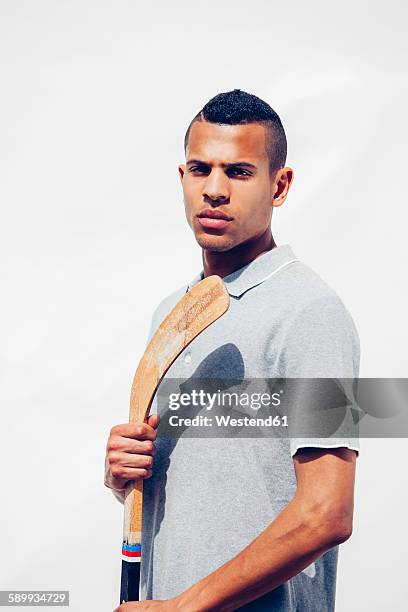 portrait of serious looking young man with shaved hair holding hockey stick in front of white background - hockey black white stock pictures, royalty-free photos & images