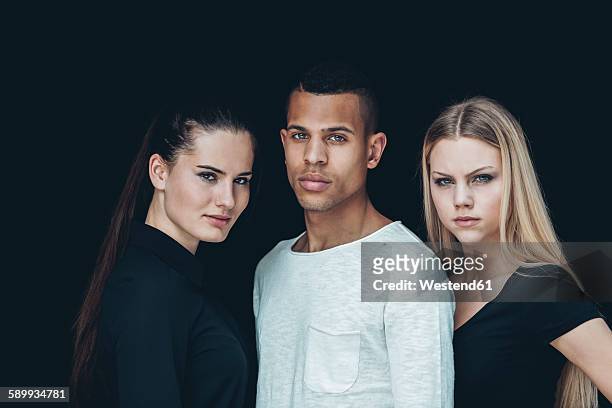 group picture of two young woman and young man in front of black background - three people portrait stock pictures, royalty-free photos & images
