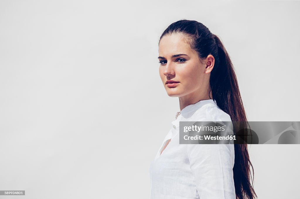 Portrait of young woman with ponytail wearing white blouse in front of white background