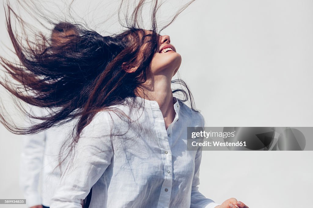 Young woman wearing white blouse tossing her long dark hair in front of white background