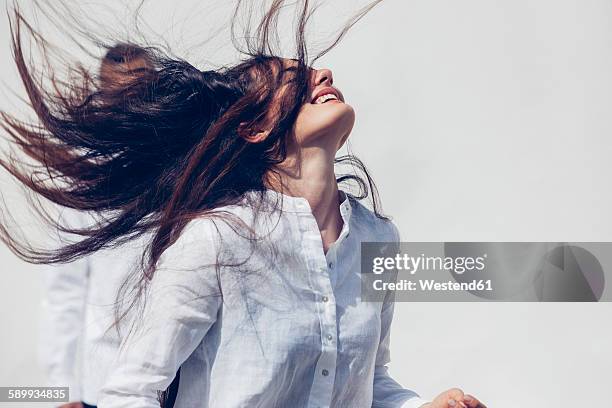 young woman wearing white blouse tossing her long dark hair in front of white background - shaking motion stock pictures, royalty-free photos & images