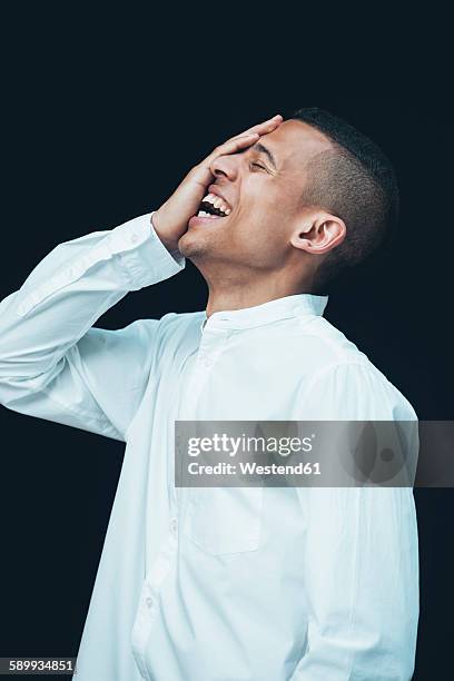 laughing young woman with hand on his face wearing white shirt in front of black background - frau lachen profil stock-fotos und bilder