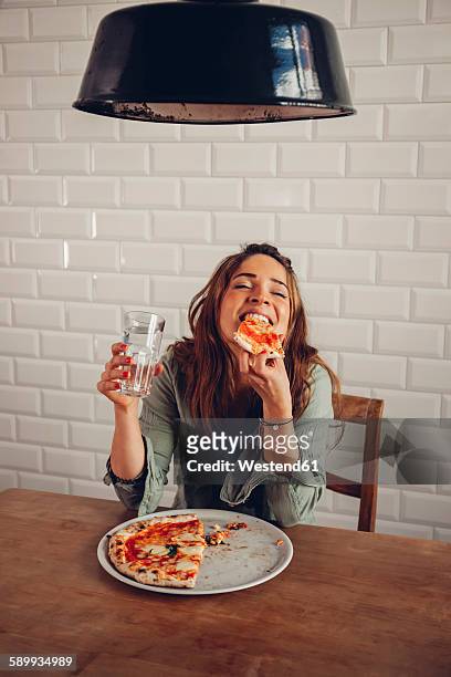 young woman eating pizza in restaurant - indulgence stock pictures, royalty-free photos & images