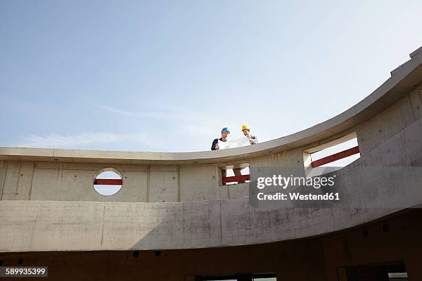 two men on construction site discussing construction plan - architekt stock-fotos und bilder