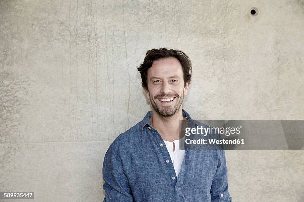 portrait of smiling man in front of concrete wall - mid adult men stock pictures, royalty-free photos & images