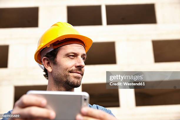 man with hard hat on construction site holding cell phone - siteseeing stock-fotos und bilder