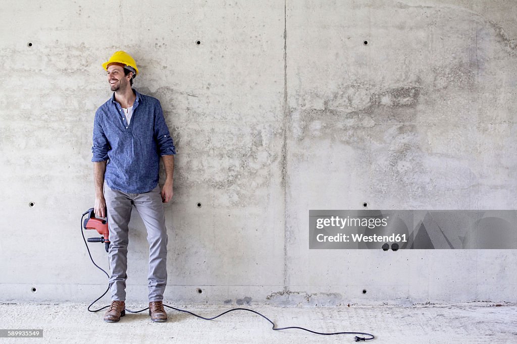 Smiling man with hard hat on construction site holding drill