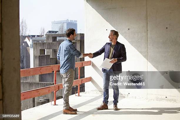 two men on construction site shaking hands - construction contract stock pictures, royalty-free photos & images