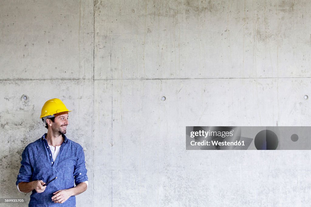 Smiling man with hard hat on construction site at concrete wall