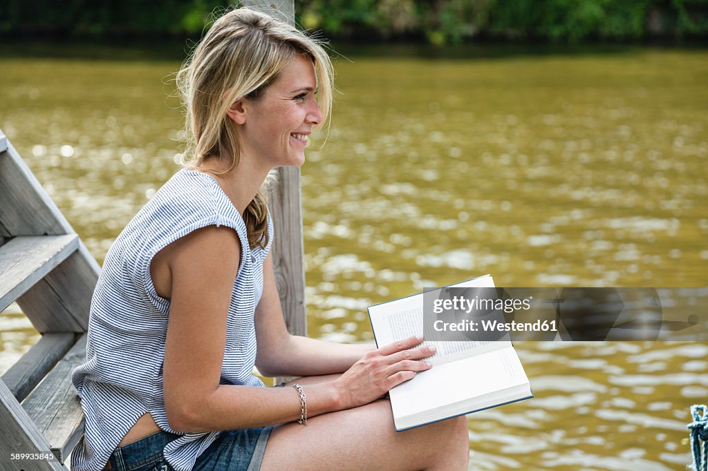 Smiling young woman reading book at the waterfront