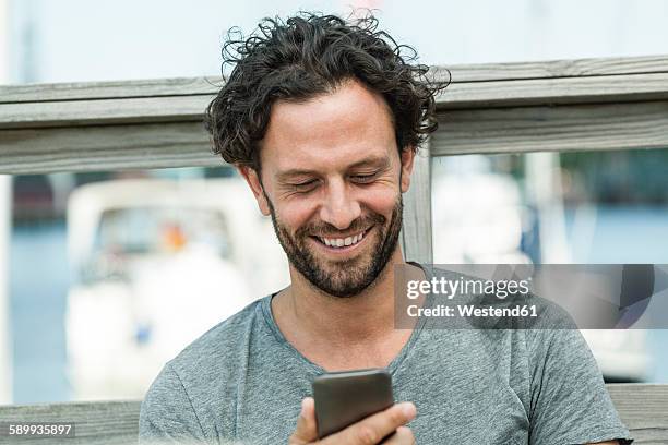 smiling man outdoors looking on cell phone - mid adult man stock pictures, royalty-free photos & images