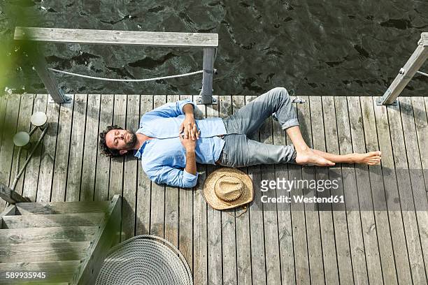 man lying on platform at the waterside - strohhut stock-fotos und bilder