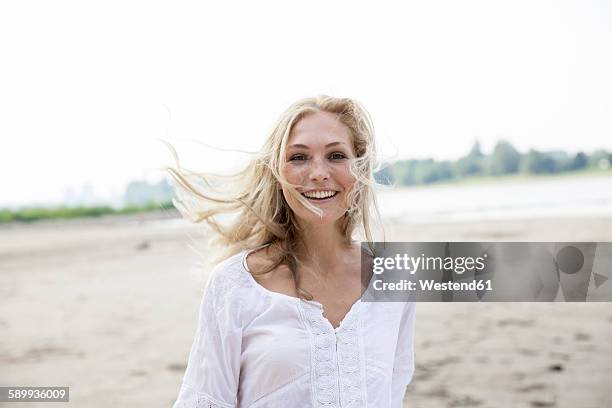 portrait of smiling blond woman with blowing hait on a beach - natural blonde stock-fotos und bilder