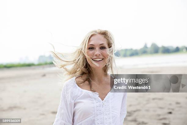 portrait of smiling blond woman with blowing hait on a beach - one young woman only foto e immagini stock