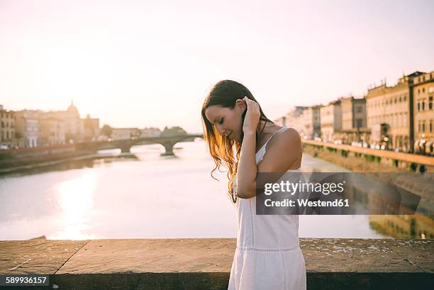 italy, florence, happy woman wearing white summer dress standing on a bridge at sunset - frau kleid stock-fotos und bilder