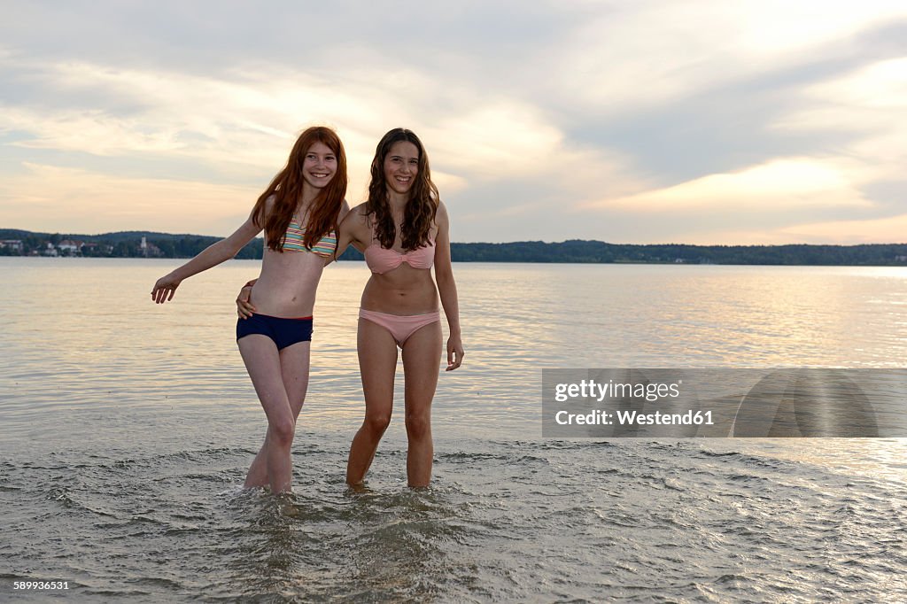 Germany, Upper Bavaria, two girls wading arm in arm in the water of Lake Starnberg