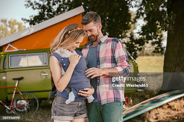 smiling couple with baby in in front of van in the nature - baby carrier stock pictures, royalty-free photos & images