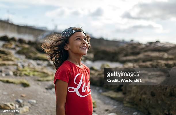 spain, gijon, portrait of smiling little girl on rocky beach looking up - african girls on beach stock pictures, royalty-free photos & images