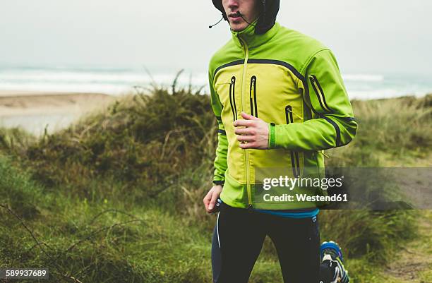 spain, valdovino, young man jogging on the beach at rainy day - green coat 個照片及圖片檔