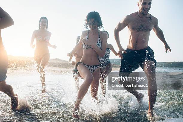 young people having fun in the sea at sunset - lens flare young people dancing on beach stock pictures, royalty-free photos & images