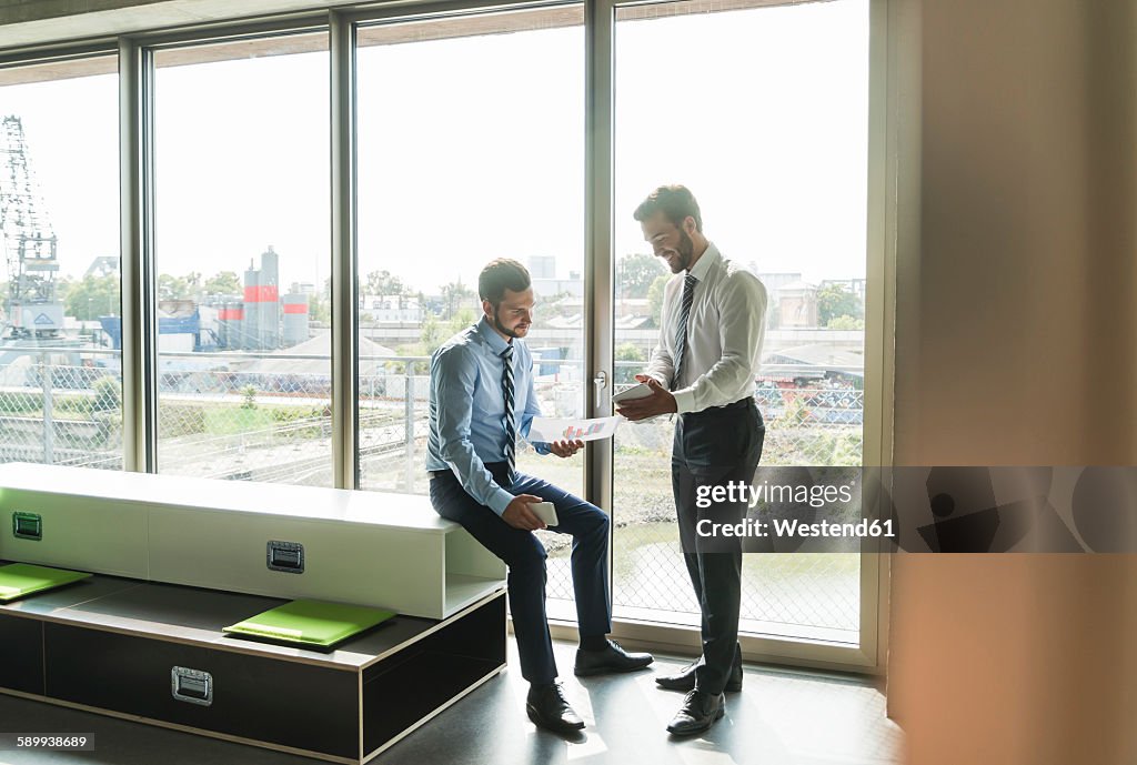 Two young businessmen looking at document and digital tablet