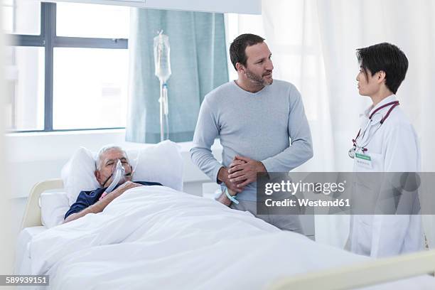 doctor talking to man visiting patient in hospital - krankenbett gespräch stock-fotos und bilder