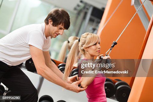 Instructor helping woman with lateral pull-down weights exercise Instructor helping woman with lateral pull-down weights exercise