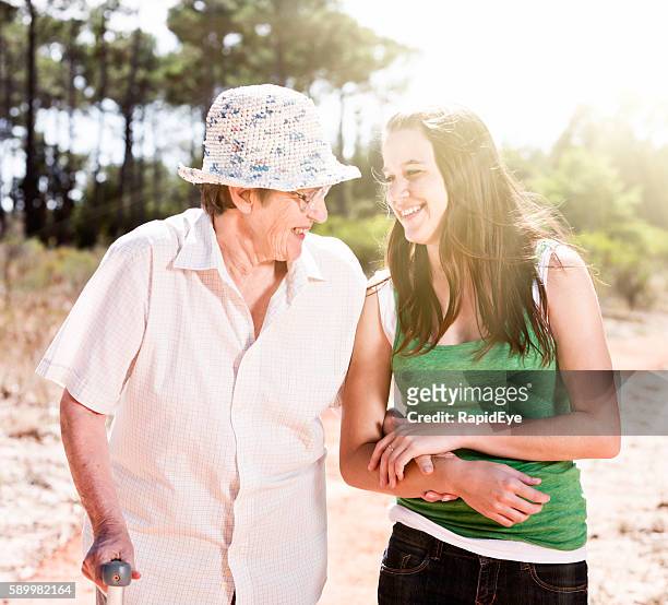 young and old woman, arm-in-arm, walk, smiling at each other - old person with walking stick outside standing stock pictures, royalty-free photos & images