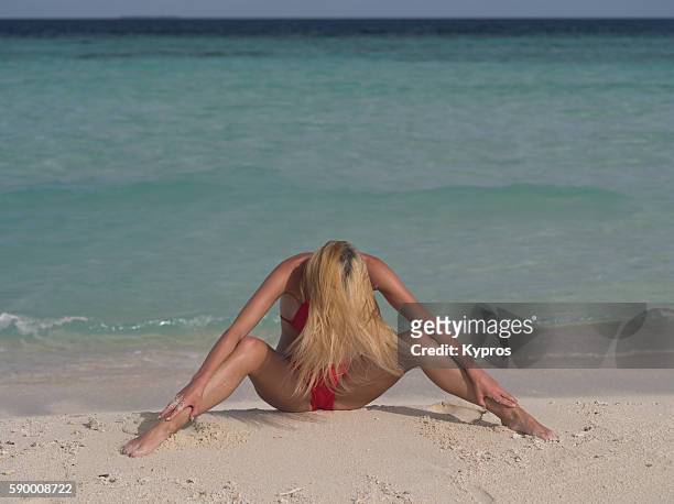 asia, maldives, young caucasian woman sitting on beach stretching her legs - risque woman foto e immagini stock