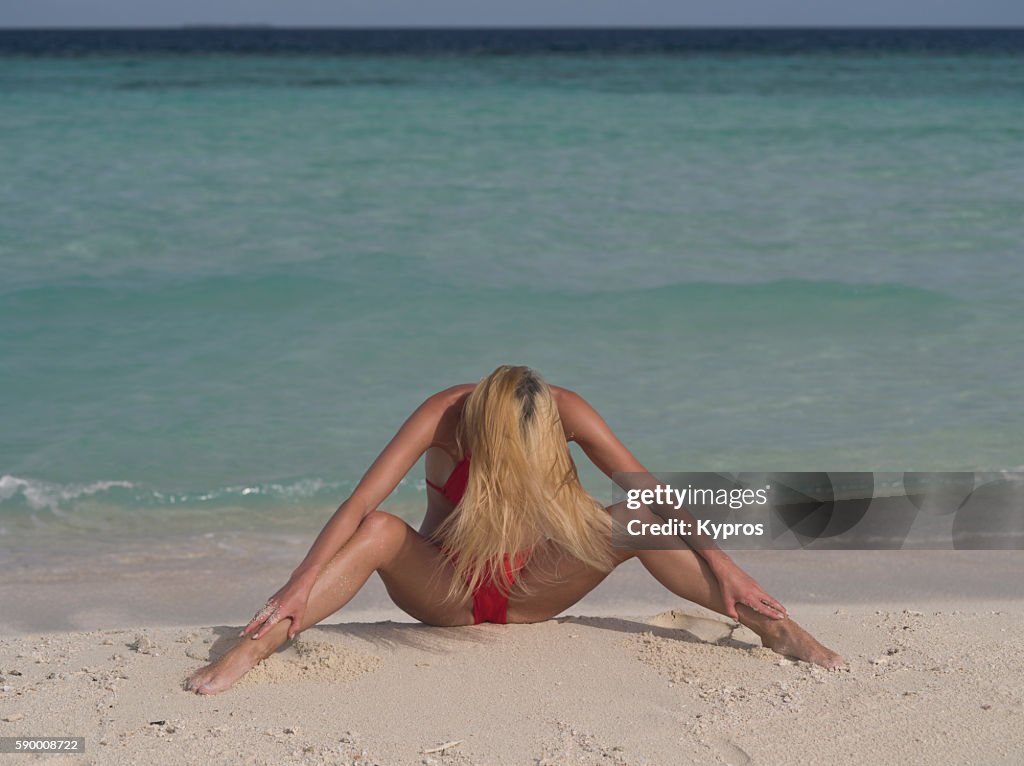 Asia, Maldives, Young Caucasian Woman Sitting On Beach Stretching Her Legs