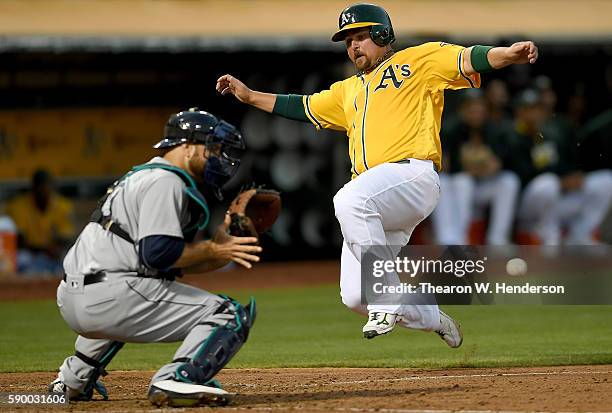 Billy Butler of the Oakland Athletics scores beating the tag of Chris Iannetta of the Seattle Mariners in the bottom of the six inning at the Oakland...