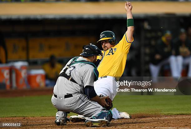 Billy Butler of the Oakland Athletics scores beating the tag of Chris Iannetta of the Seattle Mariners in the bottom of the six inning at the Oakland...