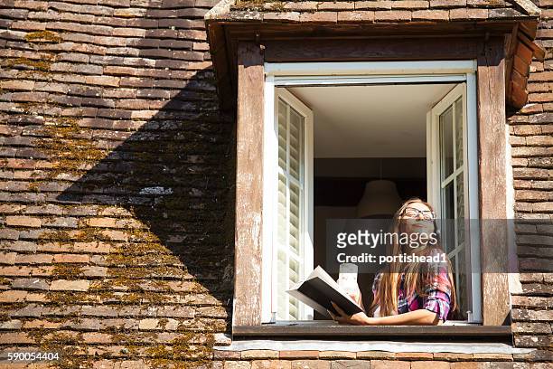 junge frau steht auf dachfenster und liest ein buch - fenster offen stock-fotos und bilder