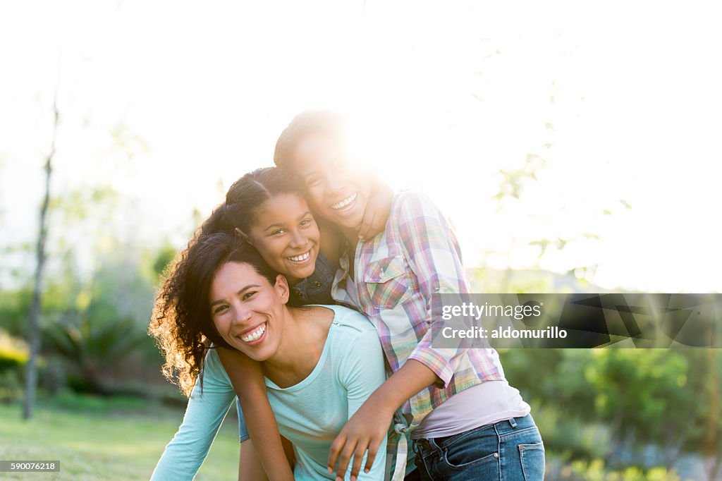 Joyful mother and daughters smiling outdoors in backlight