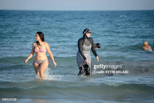 Tunisian women, one wearing a "burkini", a full-body swimsuit designed for Muslim women, swim on August 16, 2016 at Ghar El Melh beach near Bizerte,...