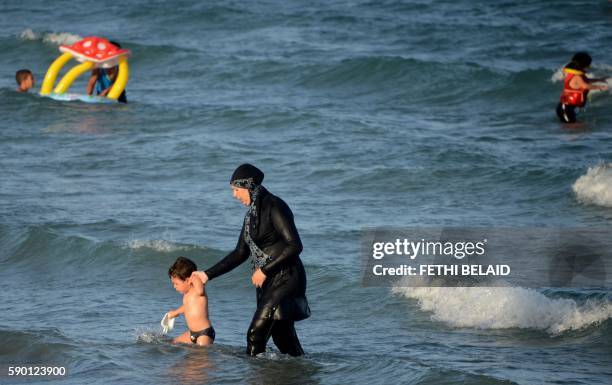Tunisian woman wearing a "burkini", a full-body swimsuit designed for Muslim women, walks in the water with a child on August 16, 2016 at Ghar El...