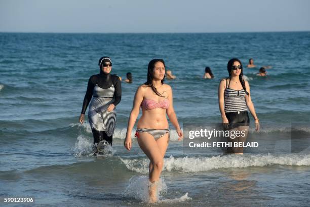 Tunisian women, one wearing a "burkini", a full-body swimsuit designed for Muslim women, walk in the water on August 16, 2016 at Ghar El Melh beach...