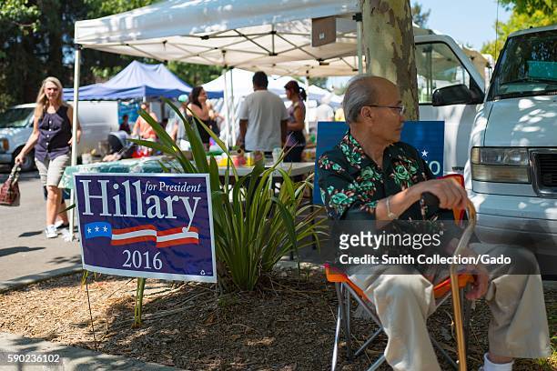 At a farmer's market in the San Francisco Bay Area town of Danville, California, a mature man with a cane sits in a chair and distributes information...