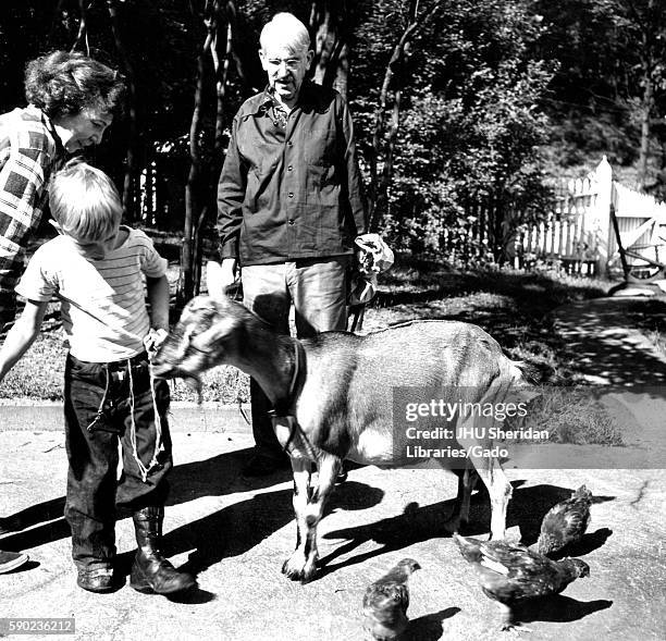 Candid portrait of American philosopher, psychologist, and educational reformer John Dewey standing on a path outside feeding a goat with his wife...