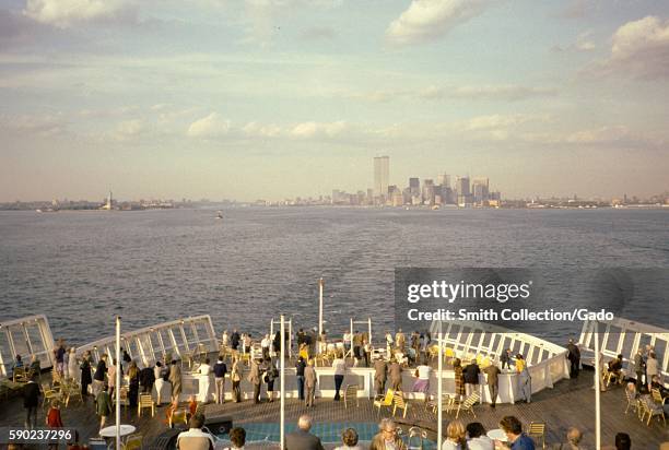 Skyline of New York City, including the twin tours of the World Trade Center, and the Statue of Liberty viewed by a group of tourists gathered on the...