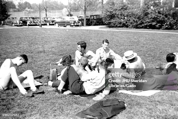 On a warm sunny day, brothers of the Delta Upsilon fraternity at Johns Hopkins University lounge in the grass on towels, shirtless while conversing...