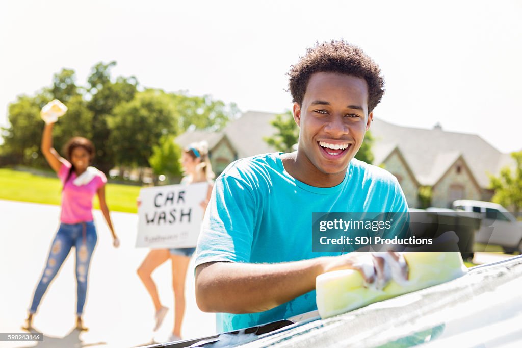 Handsome African American teenage boy washing a car